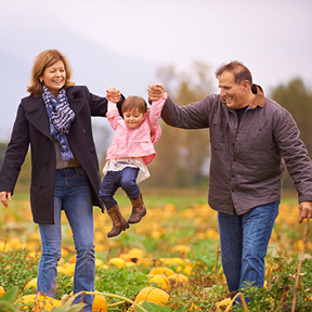 A man and woman in their fifties swinging a young girl in a pumpkin patch