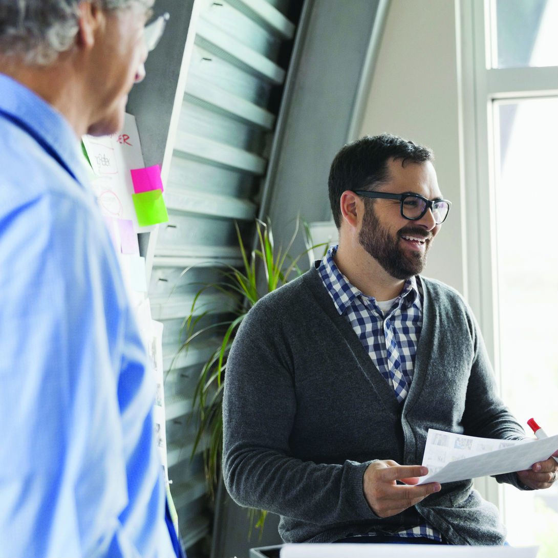 Caucasian businessman casually dressed holding a paper and marker with a coworker looking on